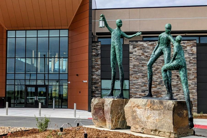 Exterior of Larimer County's Acute Care Behavioral Health facility, with three statues of people helping each other climb onto a rock