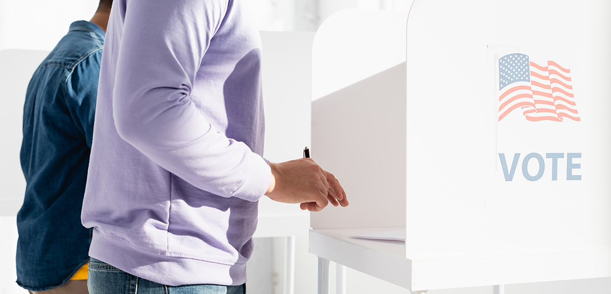 A person in a purple sweater holding a pen at a voting booth