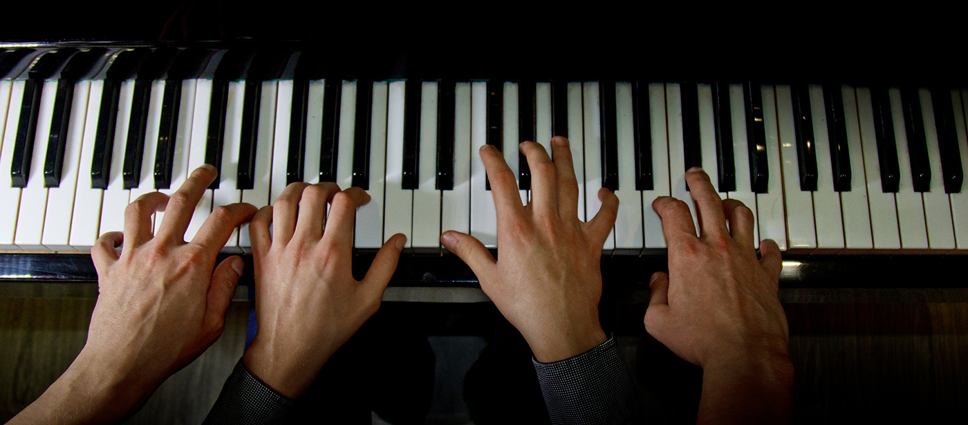 Close-up of a piano keyboard with a child's hands on the keys and an adult's hands on either side of the child's