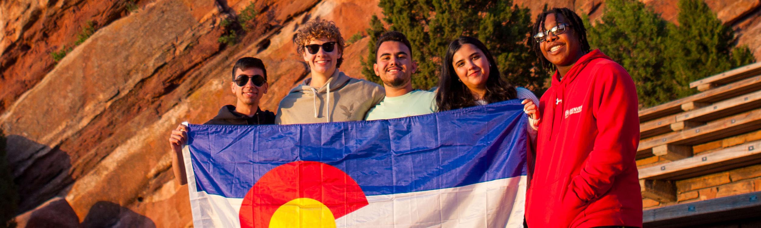 A group of young people holding the Colorado flag at Red Rocks amphitheater