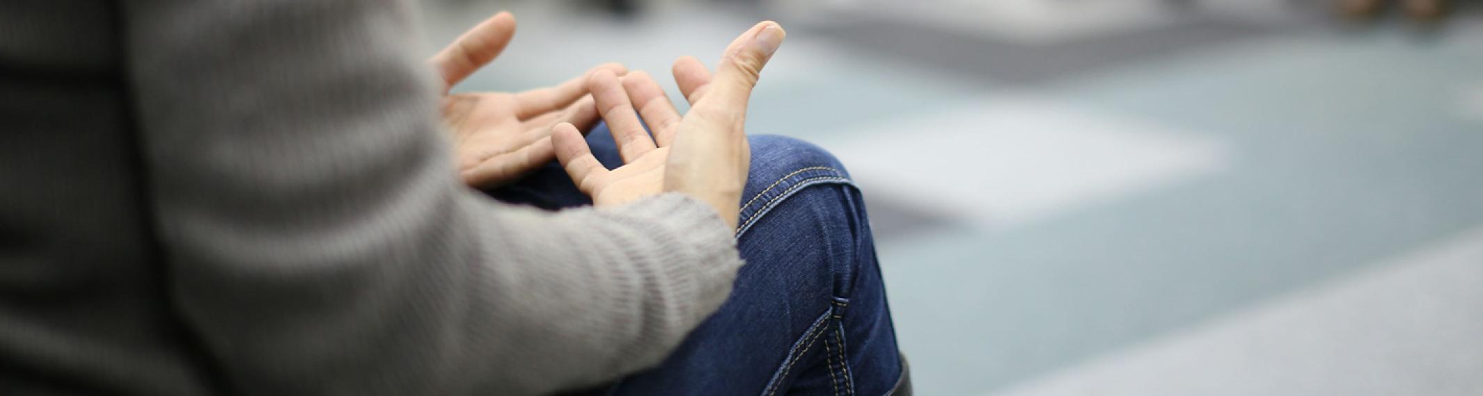 Closeup of a person's hands palm up on his lap as he talks during a group therapy session