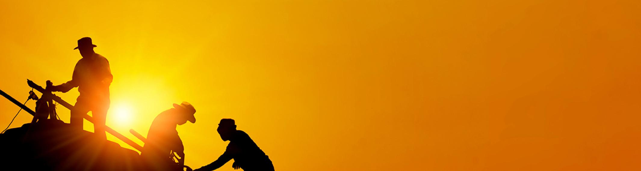 Silhouette of three workers on a roof against the setting sun and an orange sky