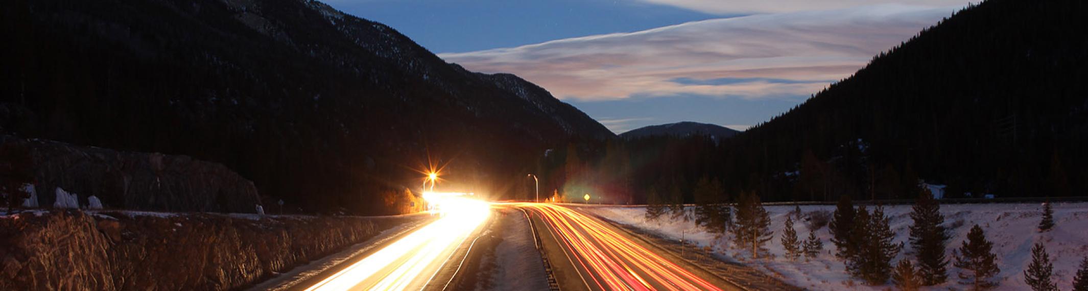 Two lanes of a highway in the mountains at sunset with blurred headlights and taillights
