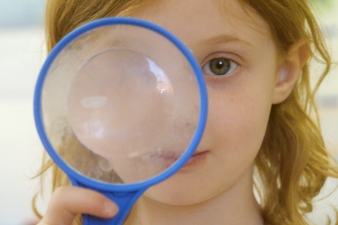 A preschool girl looking through a magnifying glass
