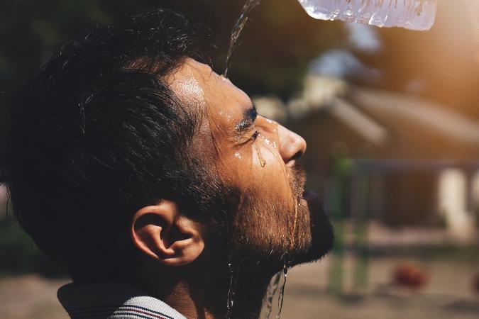 A man closes his eyes and tilts his head up while pouring water over his face to wash off sweat.