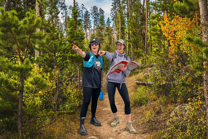 Two women on a forest trail pointing past the camera