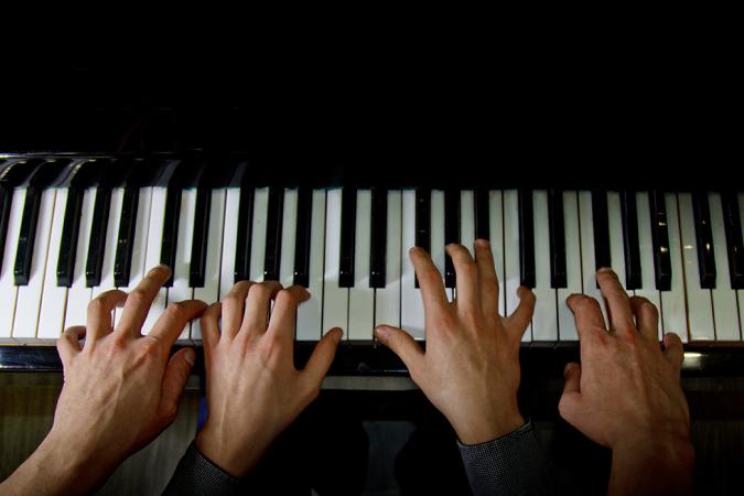 Close-up of a piano keyboard with a child's hands on the keys and an adult's hands on either side of the child's