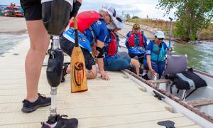 Marc Hoffmeister assists Bill Drummond into in the Team Blue dragon boat while Gary Verrazono and Honey Hendesi adjust their positions.