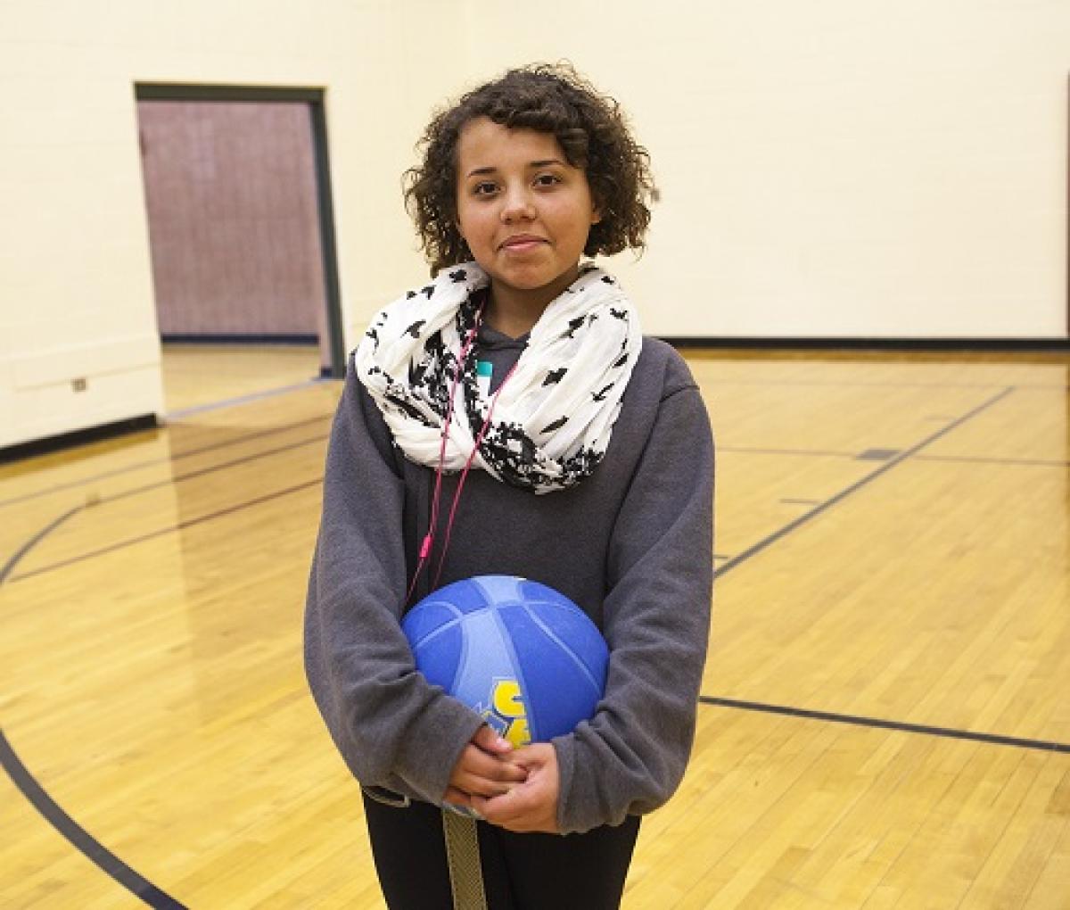 Middle-school girl poses with basketball on the court