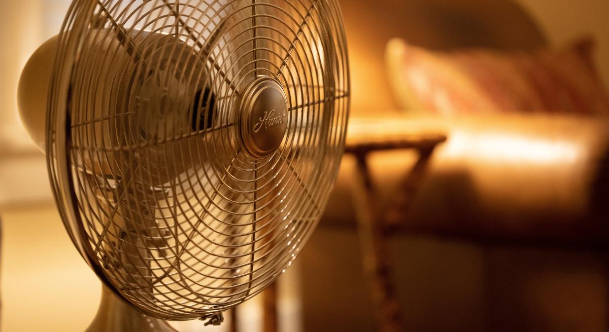 A small fan running in a room with an easy chair and side table in he background