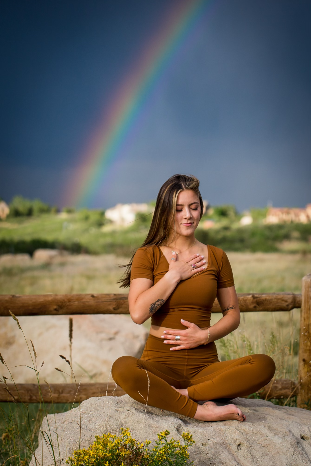 Kristen, a yoga instructor, meditates in a nature setting with a rainbow behind her.